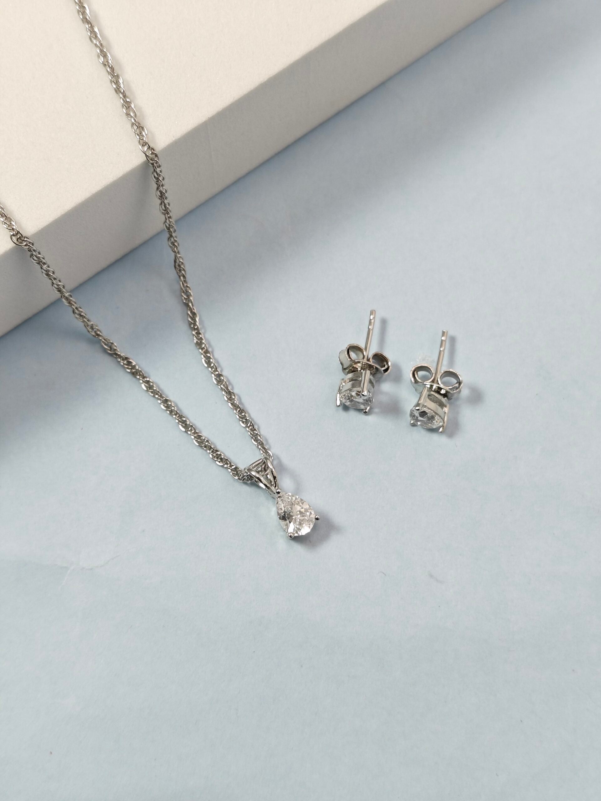 Silver necklace and earrings on a light gray surface